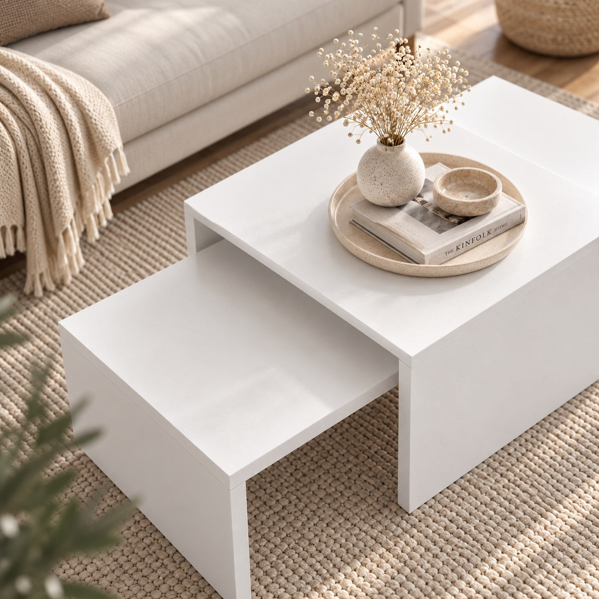 Table basse blanche design vue en plongée, avec tables gigognes et décoration épurée dans un salon beige.