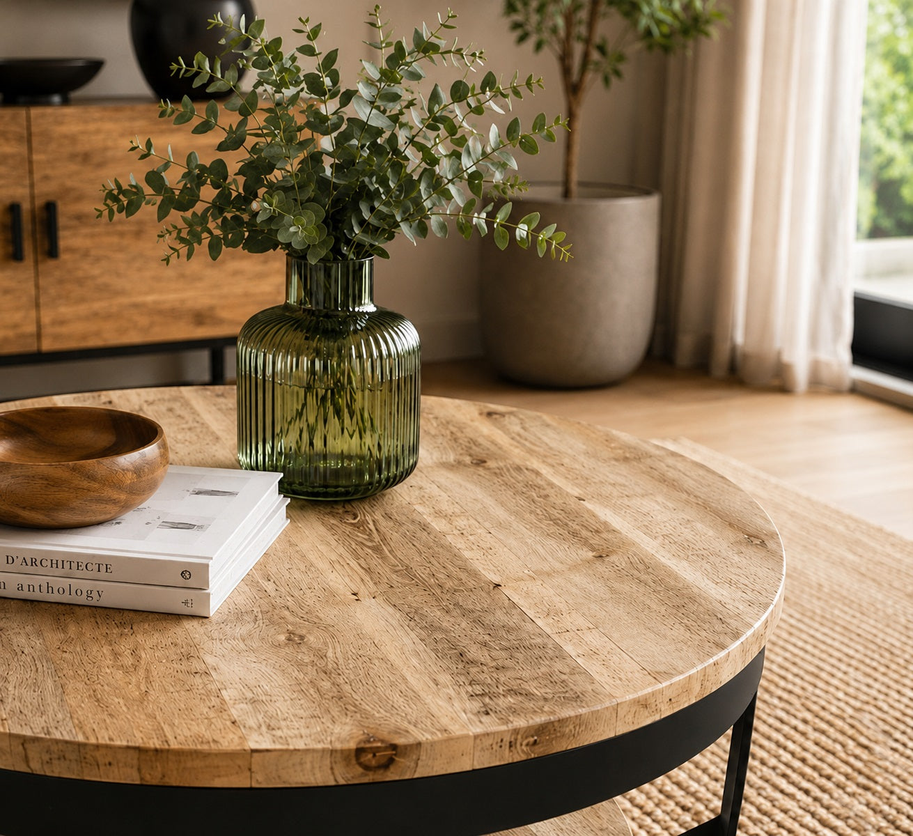 Gros plan sur table basse ronde en bois naturel avec vase vert et finition métal noir dans salon élégant