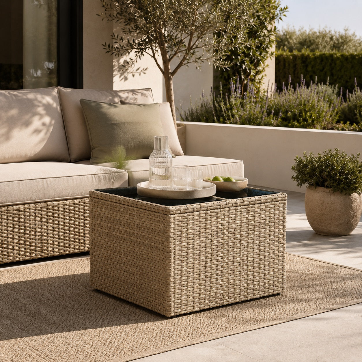 Table basse de jardin tressée beige avec plateau en verre dans un salon d’extérieure chaleureux et élégant.