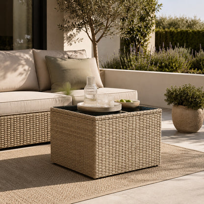Table basse de jardin tressée beige avec plateau en verre dans un salon d’extérieure chaleureux et élégant.