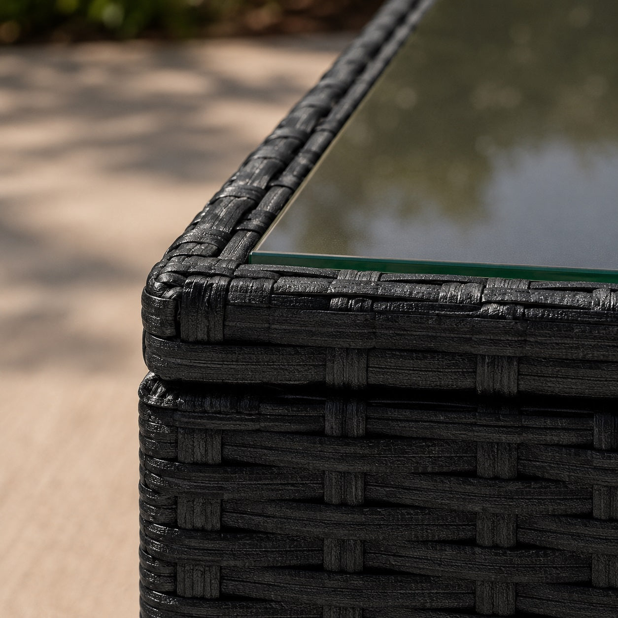 Gros plan d'une table basse de jardin en résine tressée noire avec plateau en verre, mettant en valeur la texture du mobilier.
