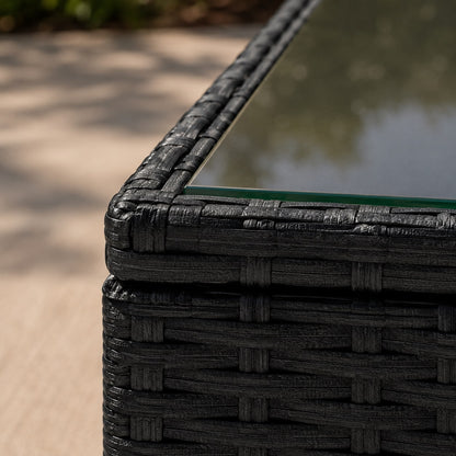 Gros plan d'une table basse de jardin en résine tressée noire avec plateau en verre, mettant en valeur la texture du mobilier.