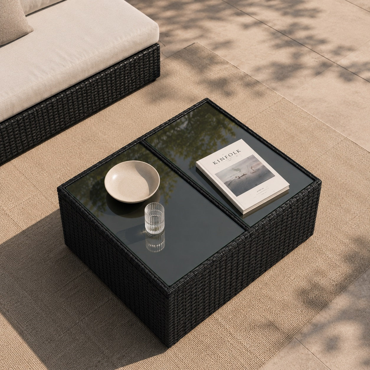 Vue en plongée d'une table basse de jardin en résine tressée noire avec plateau en verre sur une terrasse élégante.