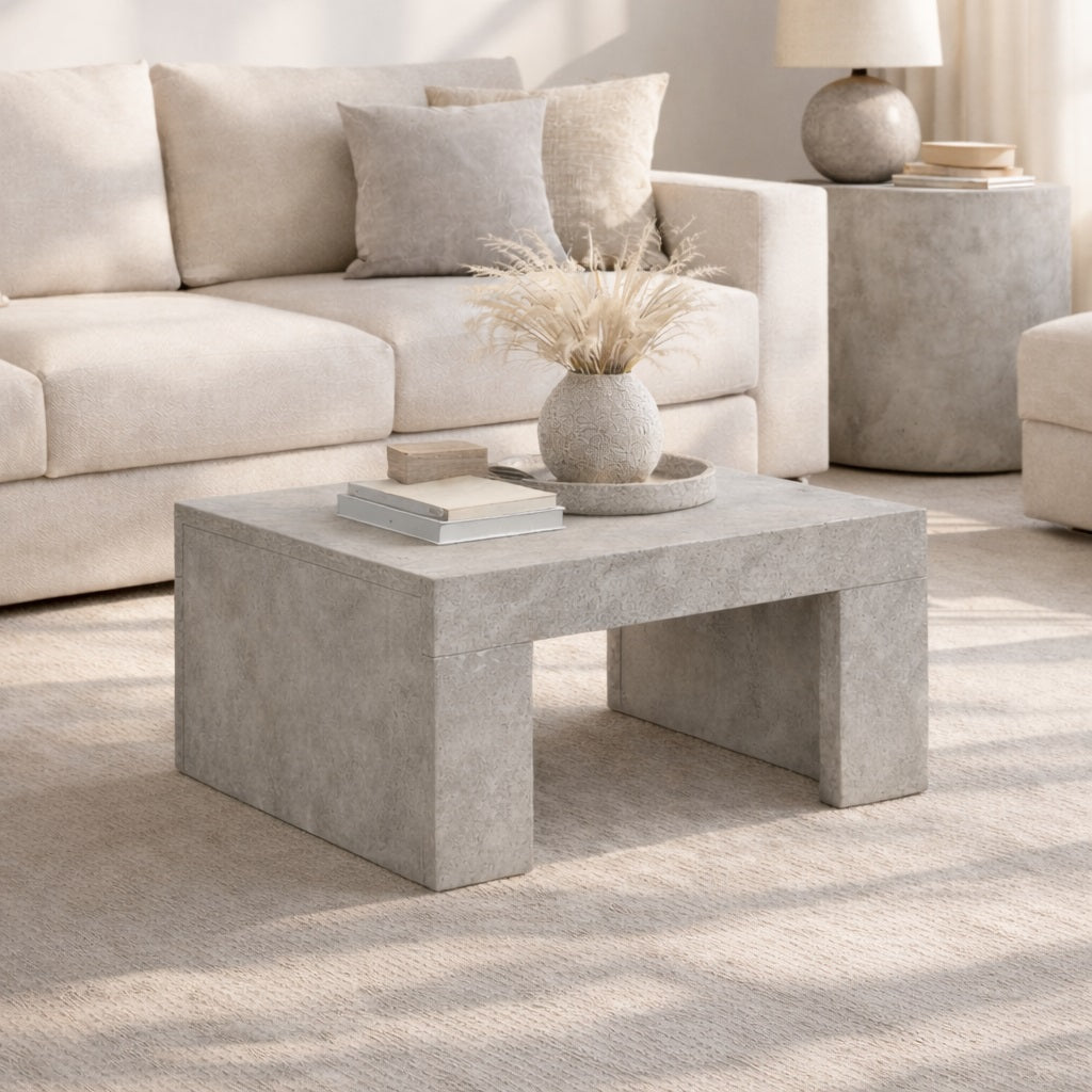 Table basse grise de salon en finition minérale, posée devant un canapé clair dans une ambiance élégante et contemporaine.